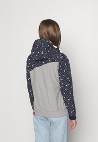 Hooded jacka med ärmar i marinblå blommönster, grå kropp, elastisk nederkant och en dragsko i huvan. Tyget verkar mjukt och strukturerat.