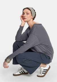 Szara bluzka z długim rękawem, luźne granatowe spodnie i białe trampki z czarnymi paskami. Dodatki to srebrne bransoletki i fakturowana szara opaska na głowę.