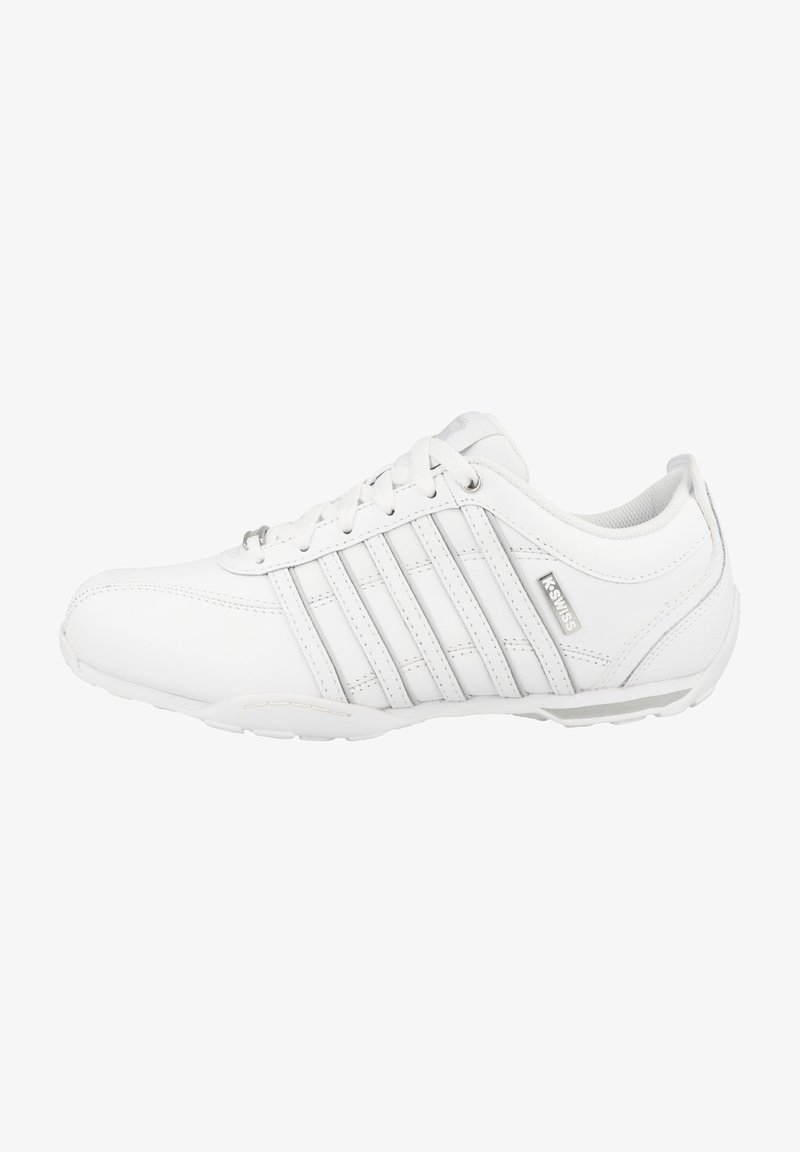 Des chaussures de sport blanches en matériau synthétique avec une texture lisse, dotées d'un design à lacets, de plusieurs rayures verticales et d'une semelle en caoutchouc.