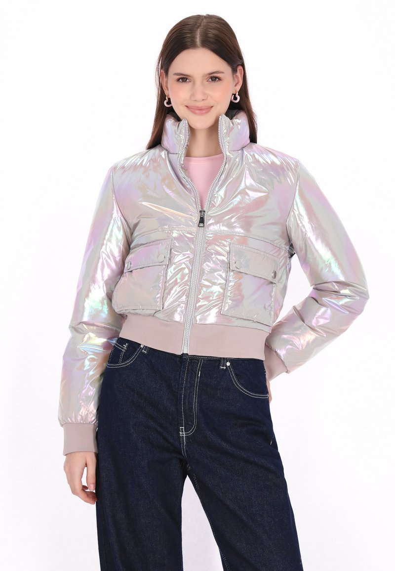 Irydescentna kurtka bombowiec z wysokim kołnierzem, zamkiem błyskawicznym z przodu, dwoma kieszeniami na piersi oraz ściągaczami przy mankietach, połączona z ciemnoniebieskimi dżinsami.