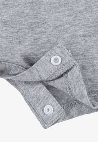 Šedá bavlněná tkanina s jemnou strukturou, která má knoflíkové ramenní patentky a zesílené švy na spodním okraji a okrajích.