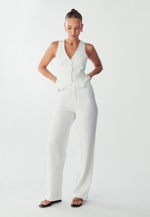 White vertical striped sleeveless top with a v-neck and button closure, paired with wide-legged, matching pants and black flat sandals.