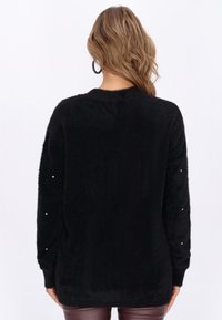Black plush sweater featuring a soft texture, long sleeves with small decorative jewels on the cuffs, and a relaxed fit design.