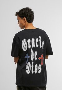 Zwarte katoen t-shirt met opvallende witte letters "Gracias de Dios" en decoratieve rode en blauwe kruisaccenten op de achterkant.