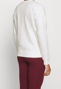 Felpa bianca con maniche lunghe, polsini e vita a costine. Tessuto liscio. Abbinata a leggings bordeaux.