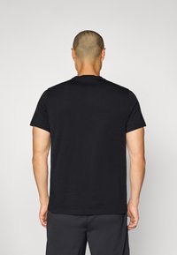 Sort bomulds t-shirt med korte ærmer og rund halsudskæring, der har en ensfarvet og afslappet pasform, set fra ryggen.