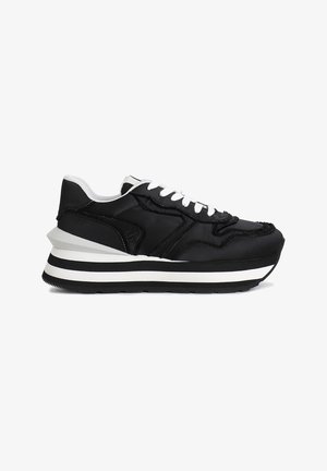 Sneaker nera con tomaia testurizzata, lacci bianchi e suola rialzata e stratificata con strisce bianche e nere. Dettaglio del logo laterale incluso.