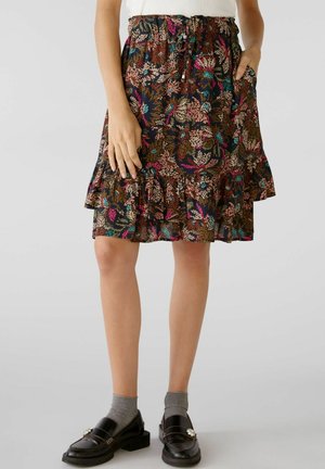 Femme portant une jupe mi-longue à imprimé floral coloré, associée à des chaussettes grises et des mocassins noirs ornés.