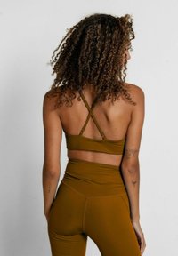 Sostén deportivo verde olivo con tirantes cruzados, combinado con leggings de cintura alta en el mismo color; textura suave y diseño ajustado.