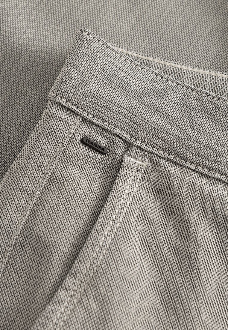 Nahaufnahme von hellgrauem Stoff mit strukturiertem Gewebe, passendem Nähten und einem schwarzen Logotag. Details des Hosensaums und der Tasche sind sichtbar.