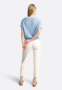 Blauwe gebreide trui met korte mouwen, textuur ontwerp; gecombineerd met witte rechte broek en bruine sleehakken.