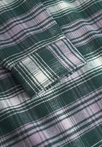Green and lavender plaid fabric with a soft texture. Features white and dark green lines forming a check pattern. Folded edge visible.