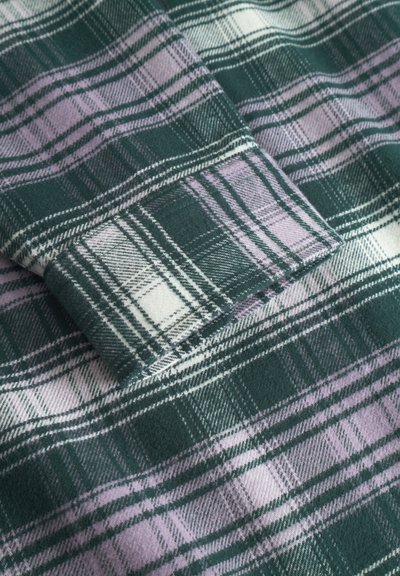 Tissu à carreaux vert et lavande avec une texture douce. Présente des lignes blanches et vert foncé formant un motif à carreaux. Bord plié visible.