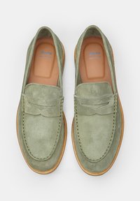 Los mocasines verdes de ante presentan una puntera estilo mocasín, detalles de costura y una suela de cuero color marrón, ofreciendo un diseño elegante y cómodo.