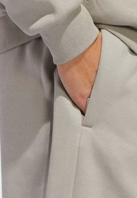 Helle graue Sweatpants aus glattem Material, mit einer Seitentasche und gerippten Bündchen, die eine weiche Textur und ein minimalistisches Design zeigen.
