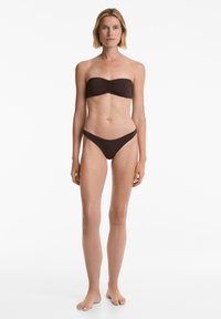 Hnědý bikiny bez ramínek s nařaseným předním detailem; vršek je bandeau stylu a spodek má nízký pas a minimální krytí.