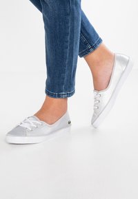 Baskets en toile argentées avec lacets blancs, design profil bas, bout arrondi et petit logo en accent. Portées avec un jean bleu raccourci.