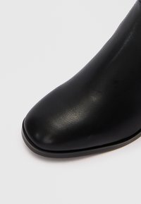 Botină din piele neagră, cu vârf ascuțit, textură netedă și un design minimalist, având o talpă plată.