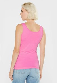 Fitted rosa Tanktop aus weichem Stoff, mit rundem Halsausschnitt und breiten Trägern, kombiniert mit lässigen blauen Jeans.