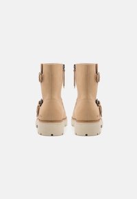 Botas de tobillo impermeables en color marrón claro, con material de ante suave, suela de goma elevada y detalles de hebilla a los lados; cierre de cremallera en la parte trasera.