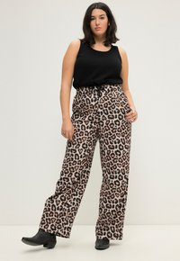 Weite Hosen mit einem Leopardenmuster in Brauntönen und Schwarz. Kombiniert mit einem schwarzen ärmellosen Top und schwarzen Stiefeln.