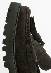 Scarpa mocassino in camoscio nero con suola spessa in gomma verde. Presenta dettagli con nappine e cuciture decorative lungo i bordi.