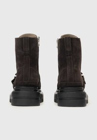 Brązowe zamszowe botki za kostkę z zamkiem błyskawicznym, czarną grubą podeszwą i kontrastowym paskiem z boku, z teksturowanym matowym wykończeniem.