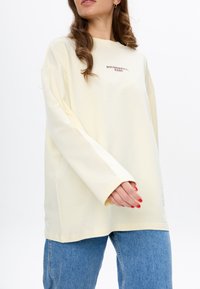 Yellow long-sleeve T-shirt with a round neckline and oversized fit, featuring maroon text "BOUNDARIES, BABE" on the front.