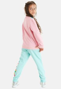 Rosa sweatshirt med turkosa detaljer, i kombination med ljusblå sweatpants som har ett färgglatt enhörningsmönster på vänster ben. Silverfärgade sneakers.