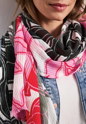 Frau trägt einen mehrfarbigen Schal mit roten, pinken, schwarzen und weißen abstrakten Mustern über einem weißen Hemd und einer Jeansjacke.