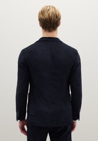 Blazer in velluto a coste blu navy con finitura texturizzata, rever a incavo e sottili linee verticali. Presenta dettagli con bottoni e una vestibilità sartoriale.
