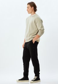 Lys beige sweatshirt med ribbet tekstur, afslappet pasform. Sorte bukser med lynlås-lomme i siden, tapered ben, parret med høje sneakers.