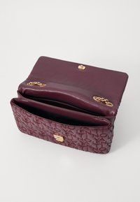 Bordo kožna torba preko ramena s utisnutim logotipom, zlatnom kopčom, lancima kao dekoracijom i unutarnjim pregradama.