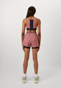 Athletic outfit featuring a pink tank top with black accents, paired with pink shorts over black compression shorts; smooth fabric, minimal design.