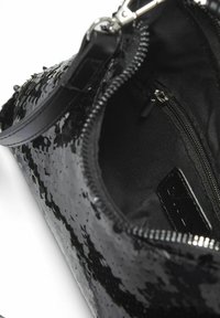Clutch bag nera in paillettes con chiusura con zip, dotata di una fodera interna liscia, piccolo taschino interno e una tracolla in pelle.