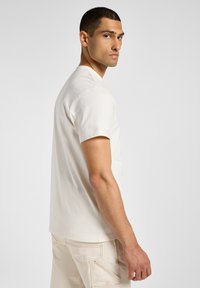 T-shirt beige in cotone a maniche corte con scollo rotondo classico, caratterizzato da una vestibilità rilassata e dettagli di cucitura minimi.