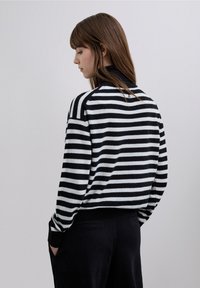 Svartvit randig tröja med hög krage, med en mjuk textur och ribbade ärmslut, visad bakifrån.