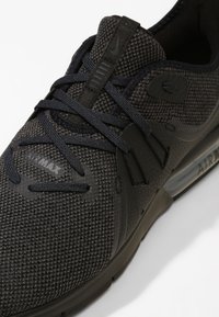 Czarne sneakersy Nike Air Max z teksturowaną siateczką u góry, płaskimi sznurowadłami oraz widoczną amortyzacją powietrzną w podeszwie. Zawierają subtelne detale brandingowe.
