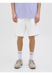 Pantalones cortos de algodón blancos con un ajuste cómodo, que presentan un corte recto y bolsillos laterales. Llevados con zapatos gris claro y calcetines blancos.