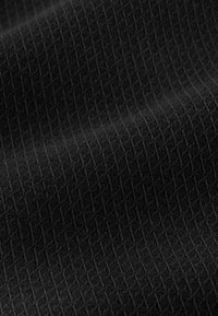 Close-up of black fabric with a textured, geometric diamond pattern and soft folds creating shadow variations.