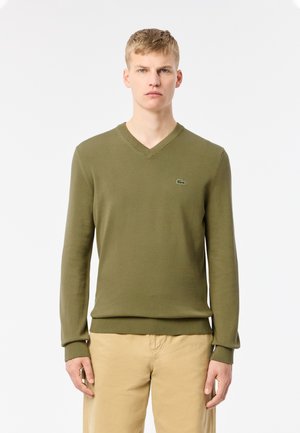 Jersey de punto verde con cuello en V, que presenta un diseño ajustado y puños y dobladillo acanalados. Logo de Lacoste bordado en el pecho.