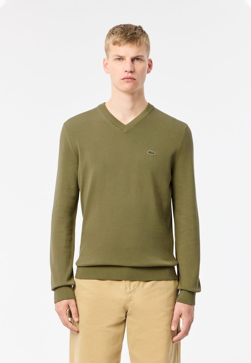 Jersey de punto verde con cuello en V, que presenta un diseño ajustado y puños y dobladillo acanalados. Logo de Lacoste bordado en el pecho.