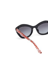 Gafas de sol de gato negro con lentes gris degradado. Patrón floral rojo en las varillas transparentes. Acabado brillante. Accesorios de hardware plateado.
