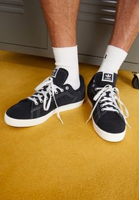 Sneakers in suede blu navy con suole e lacci in gomma bianca. Presentano una patch con logo sulla linguetta e dettagli di cuciture bianche a contrasto.