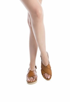 Sandalias de cuero color marrón claro con un diseño de tiras cruzadas, puntera abierta, suela beige y detalle de hebilla ajustable en el lateral. Textura suave.