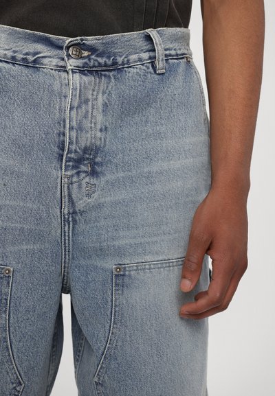 Light blue jeans made of denim with a faded texture, featuring a button waist, belt loops, and front pockets with metallic accents.