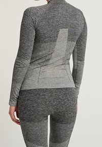 Camiseta atlética gris de manga larga con un patrón texturizado y diseño de panal. Combinada con leggings gris a juego que presentan texturas variadas.