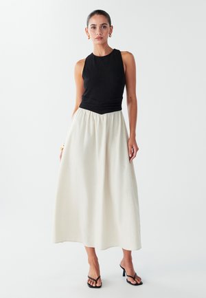 Black ribbed sleeveless top with twisted detail, paired with a long, flowing cream skirt. Model wears black strappy sandals. Smooth textures.