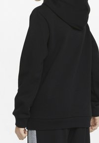 Sudadera negra con un tejido suave y texturizado, que presenta una capucha grande y puños y dobladillo acanalados. Detalles de costura sutil y un ajuste relajado.