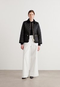 Zwarte gewatteerde jas met een kraag, voorzakken en gouden hardware, gecombineerd met brede witte broeken en grijze hakken. Glad fabricagel.